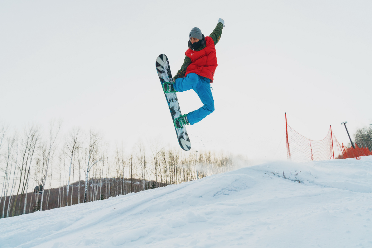 Active snowboarder jumping with raised arm above snowy mountain